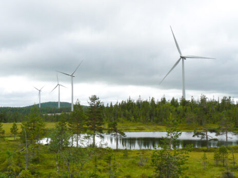 Vindsnurra i bakgrunden, med en vattenspegl framför. Foto.